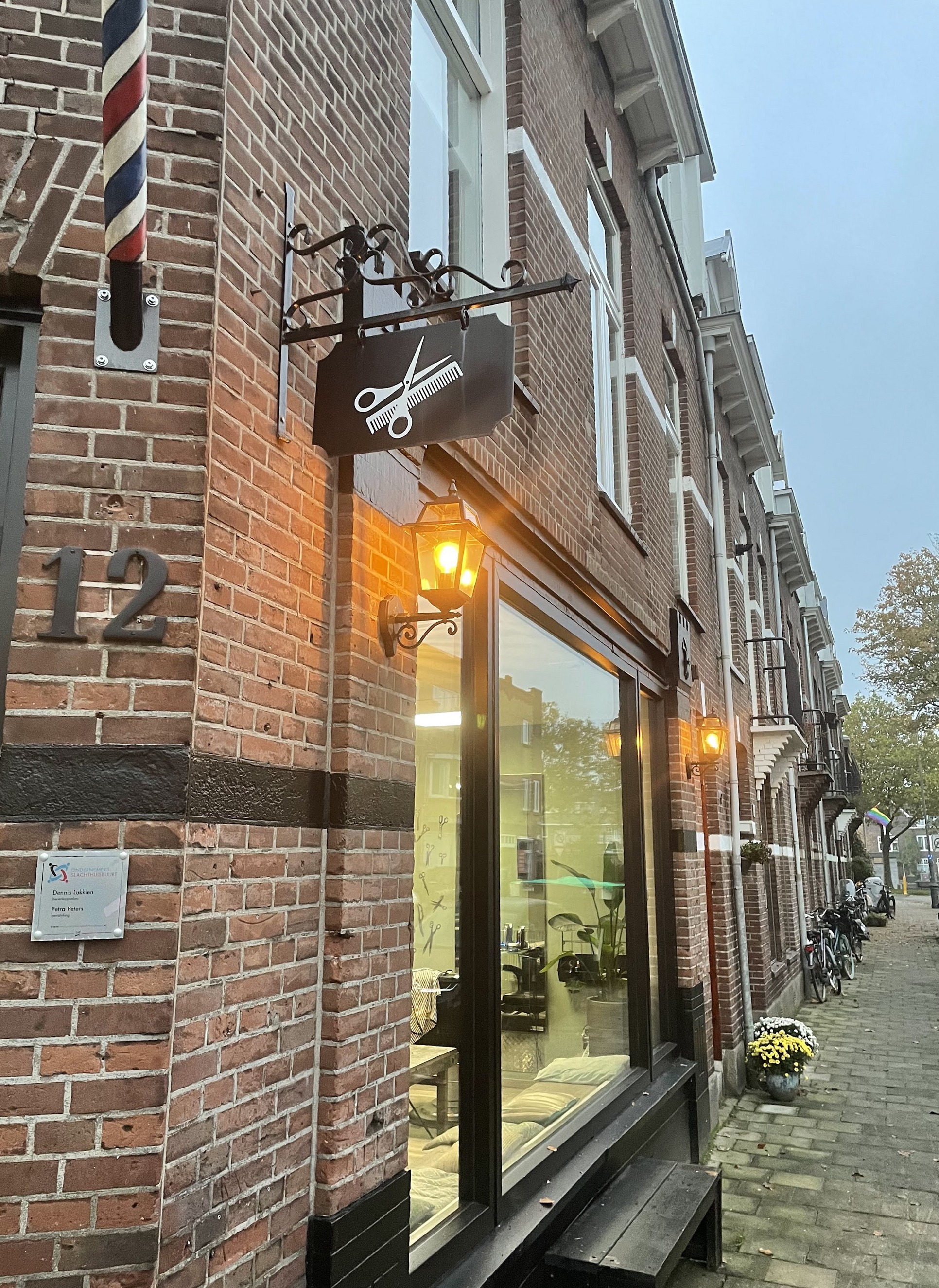 Het hoekpand van Herenkapsalon Dennis Lukkien aan de Slachthuisstraat, met de kapperspaal, het uithangbord met de schaar en huisnummer 12