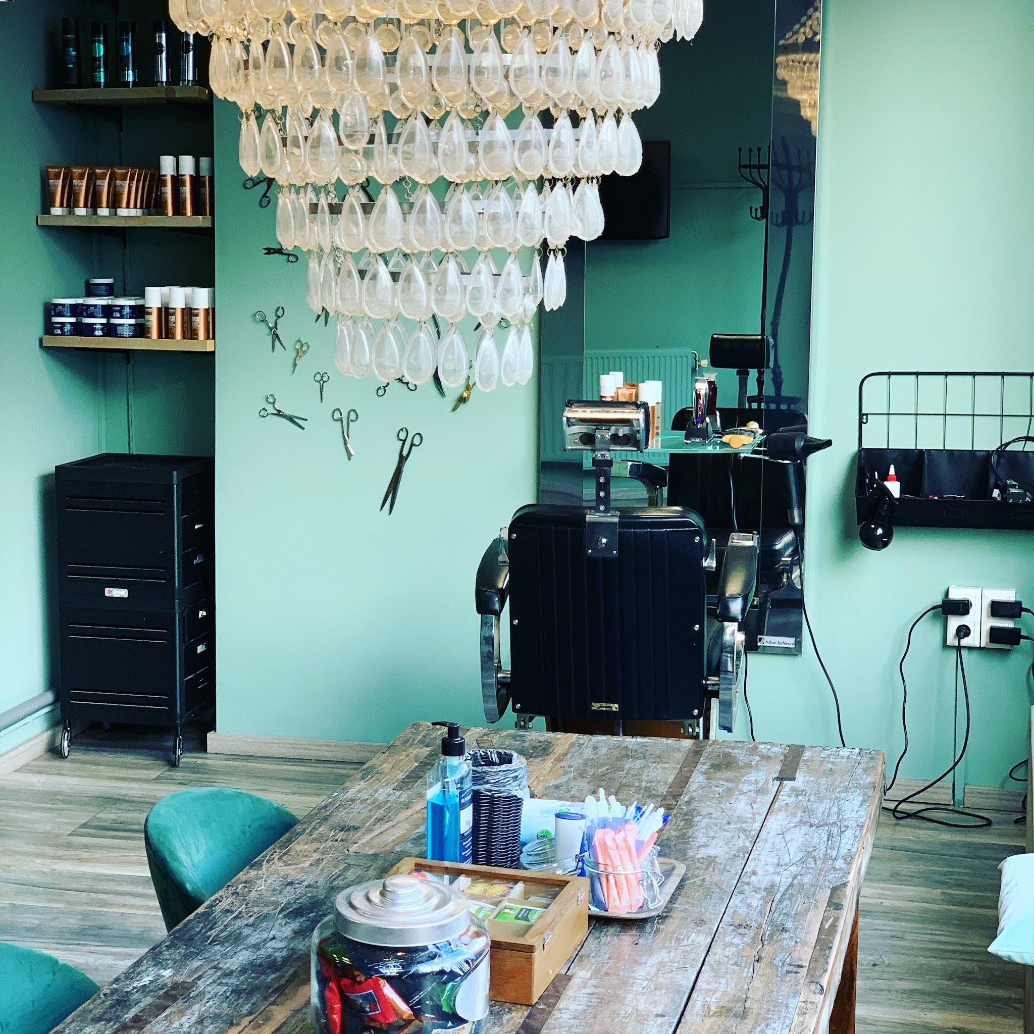 De groenblauwe wand met de kroonluchter, de kappersstoel en de houten tafel