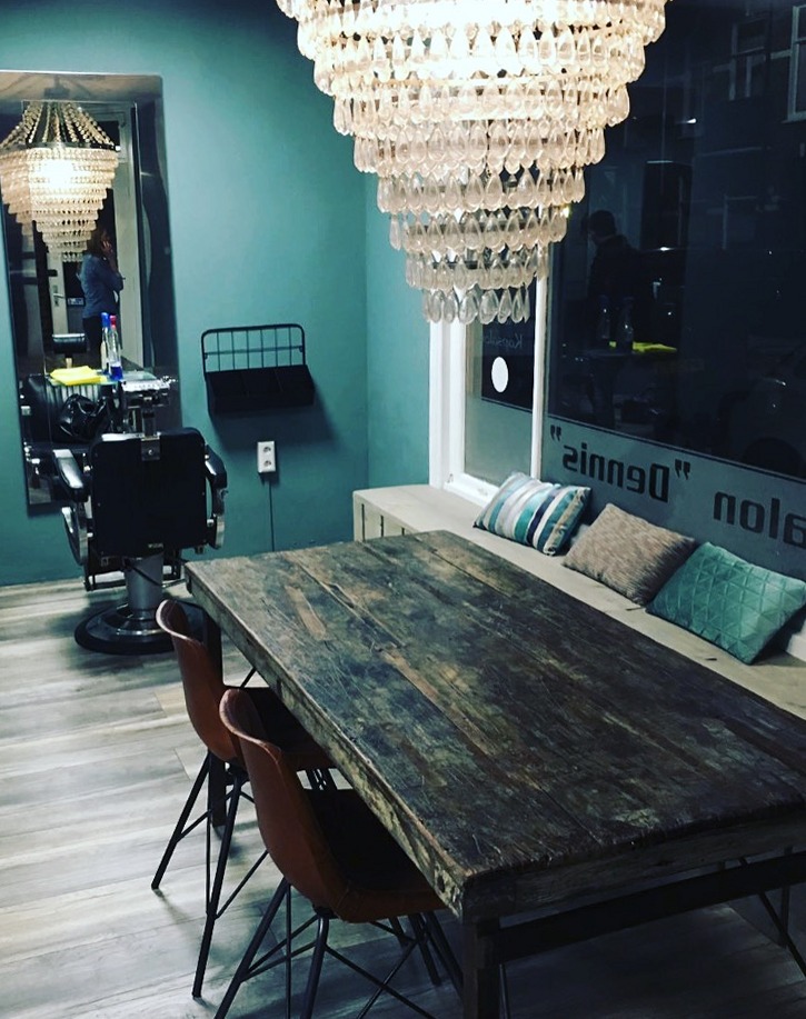 De salon bij avond, met de kroonluchter boven de tafel en de naam Dennis op het raam